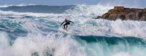 Photo of surfer in waves with rocks