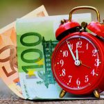 Picture of a clock with money notes next to it