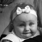 Black and white photo of an unhappy baby looking over a woman's shoulder at the camera