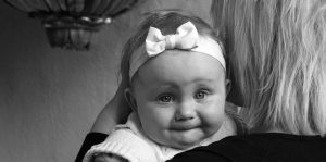 Black and white photo of an unhappy baby looking over a woman's shoulder at the camera
