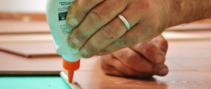 A hand holding a glue bottle and putting glue on a board