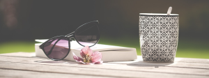 TCOY - take care of yourself. Photo of a mug, a book and a pair of sunglasses on an outside surface.